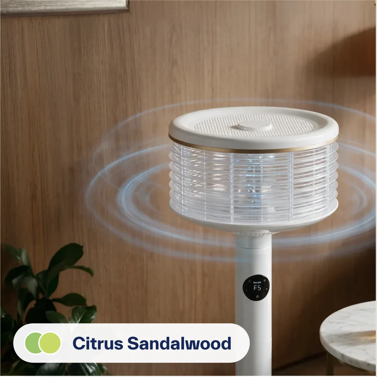 A white Spin360 against a walnut wall beside an armchair, with a drink and sandalwood chips on a marble side table. Label: Citrus Sandalwood.